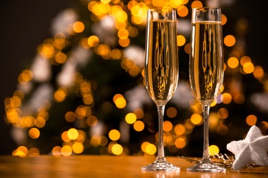 Photo of Champagne in glasses and decor on table against blurred Christmas lights, space for text. Bokeh effect