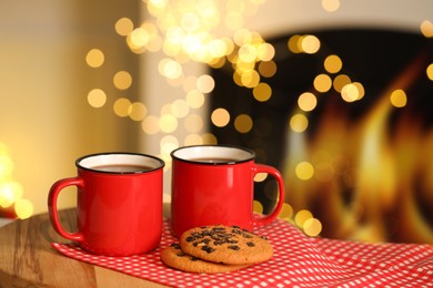 Photo of Tasty cocoa in cups and chocolate chip cookies on table against blurred Christmas lights. Bokeh effect