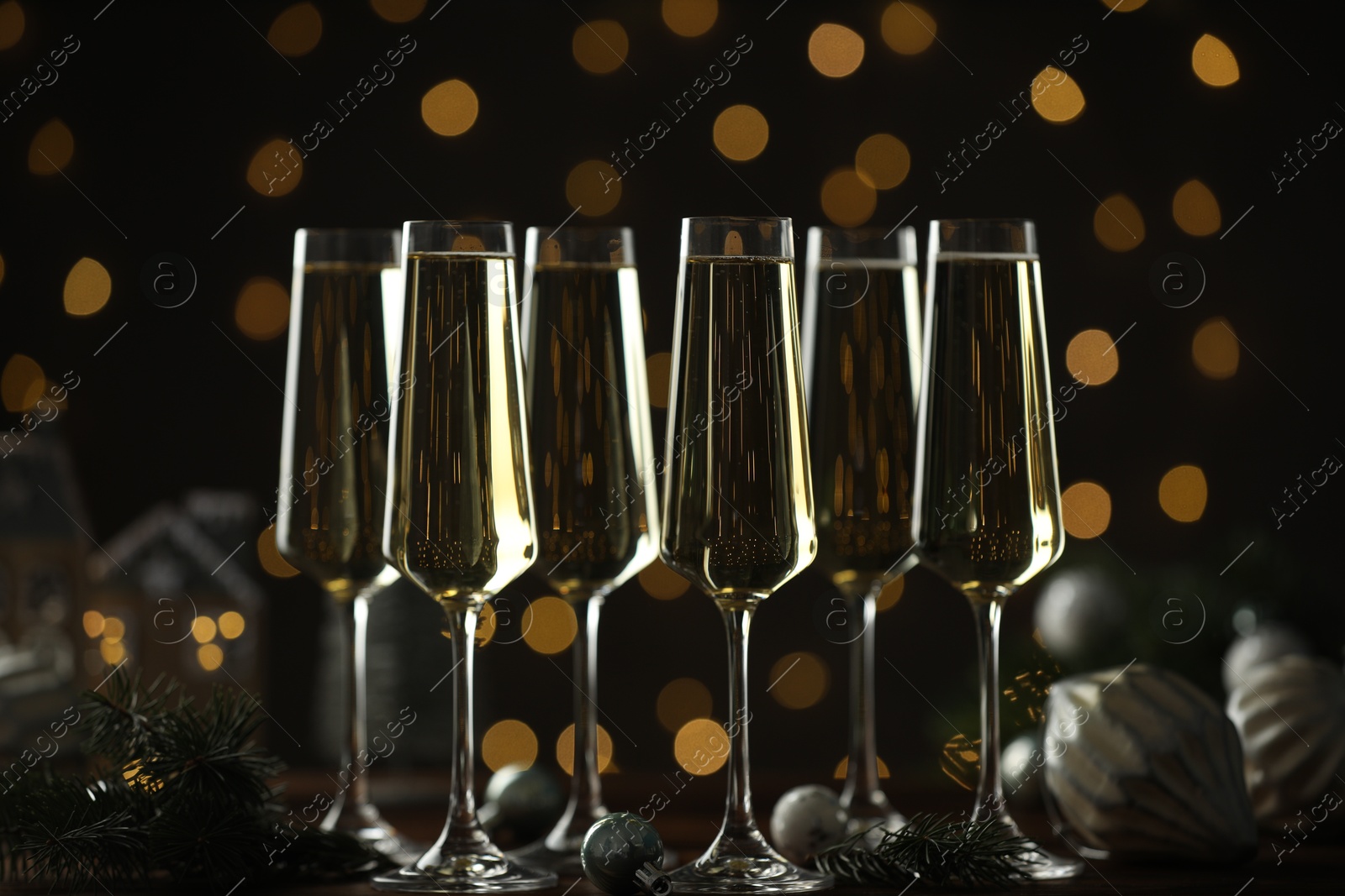 Photo of Champagne in glasses and Christmas decor on wooden table against blurred lights. Bokeh effect