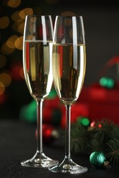 Photo of Champagne in glasses and decor on black table against blurred Christmas lights