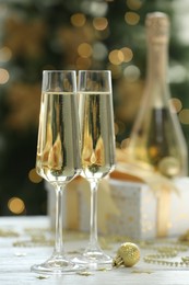 Photo of Champagne in glasses and Christmas decor on white wooden table against blurred lights. Bokeh effect