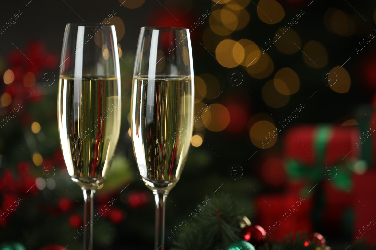 Photo of Champagne in glasses with decor against blurred Christmas lights, closeup and space for text