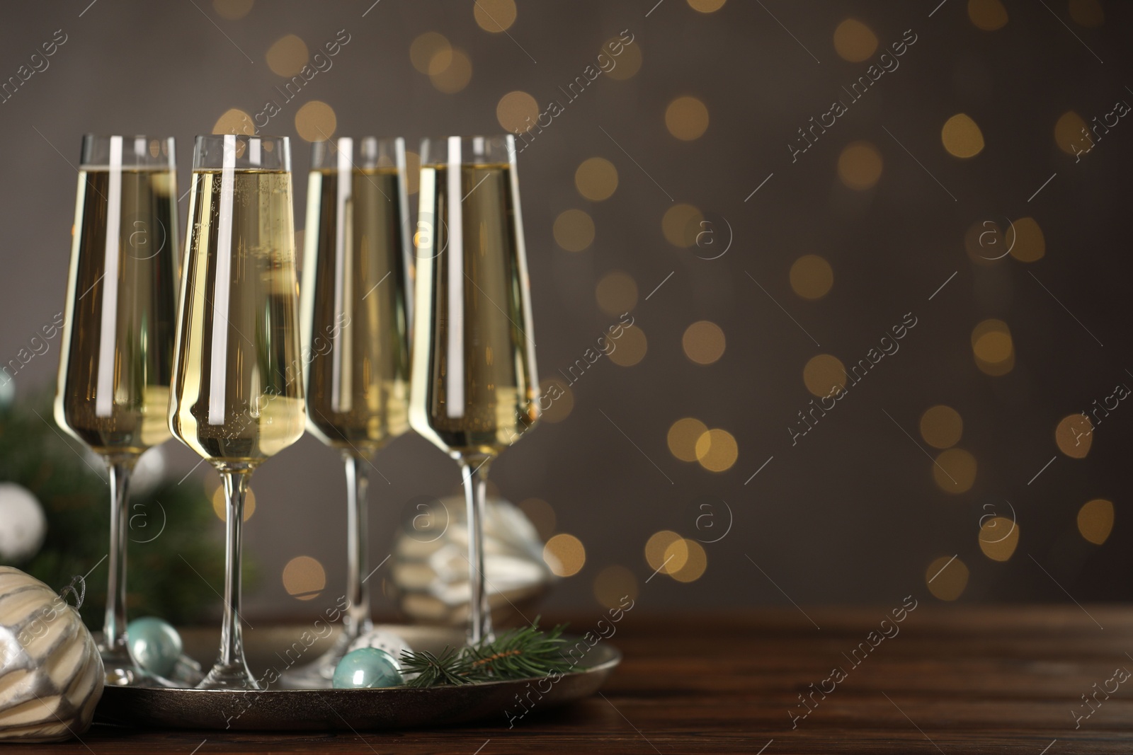 Photo of Champagne in glasses and decor on wooden table against blurred Christmas lights, space for text. Bokeh effect