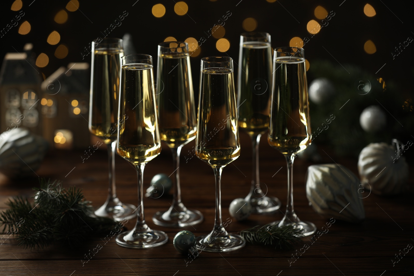 Photo of Champagne in glasses and Christmas decor on wooden table against blurred lights. Bokeh effect