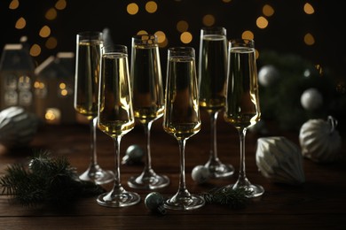 Photo of Champagne in glasses and Christmas decor on wooden table against blurred lights. Bokeh effect