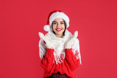 Woman in Santa hat, knitted mittens, scarf and sweater on red background. Christmas celebration