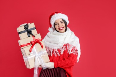 Photo of Woman in Santa hat, scarf and sweater holding Christmas gifts on red background