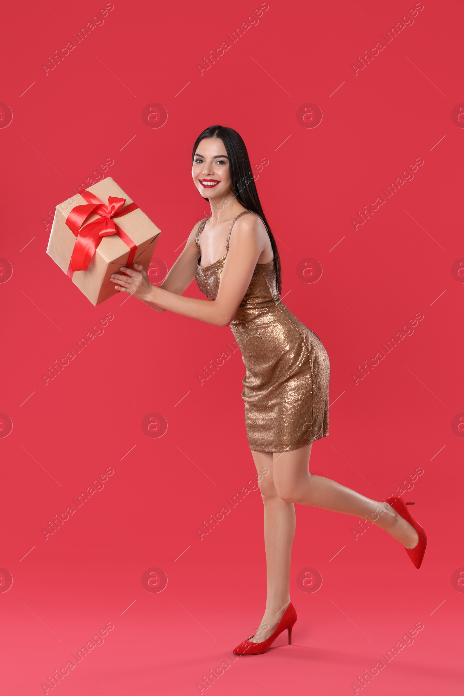 Photo of Woman in golden dress holding Christmas gift on red background