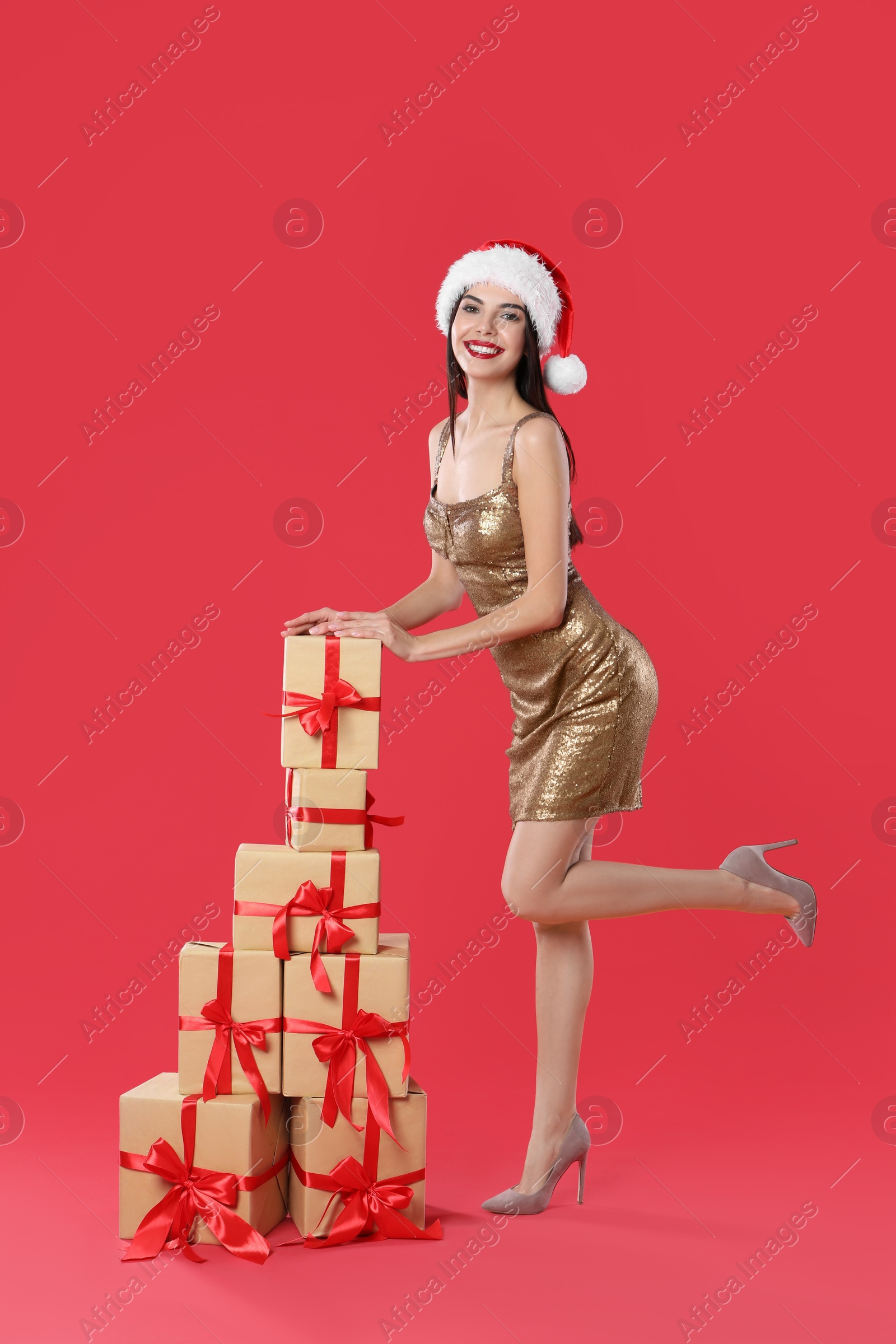 Photo of Woman in golden dress and Santa hat with Christmas gifts on red background