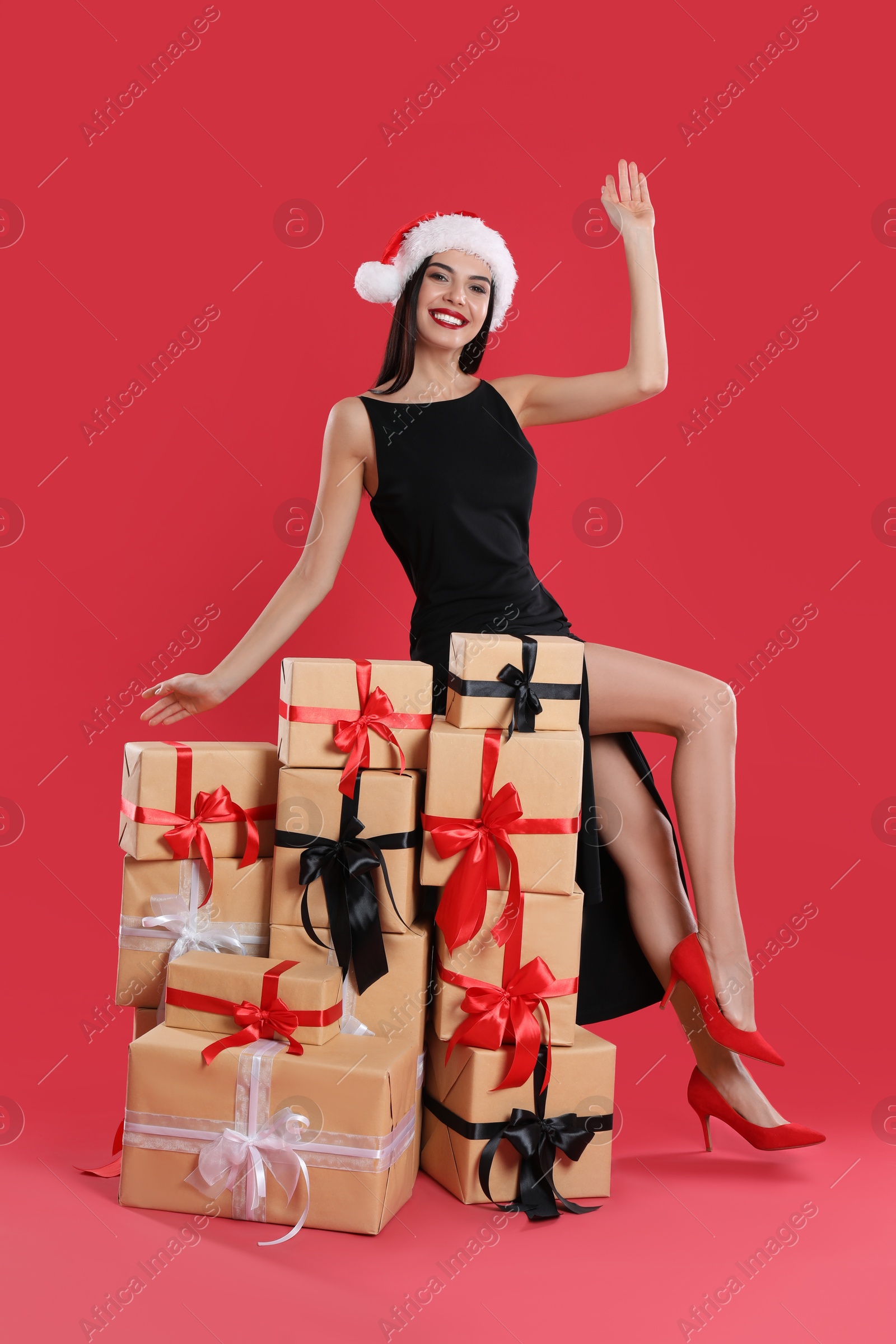 Photo of Woman in black dress and Santa hat with Christmas gifts on red background