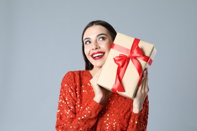 Woman in red dress holding Christmas gift on grey background