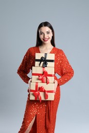 Woman in red dress holding Christmas gifts on grey background