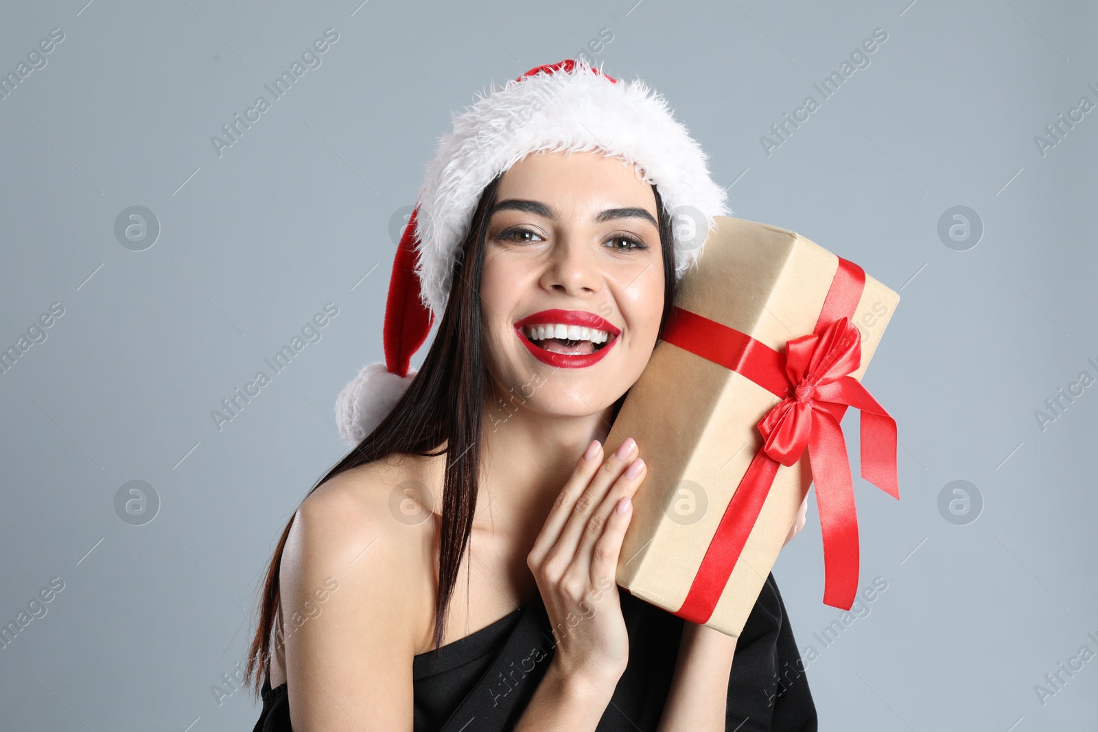 Photo of Woman in black dress and Santa hat holding Christmas gift on grey background