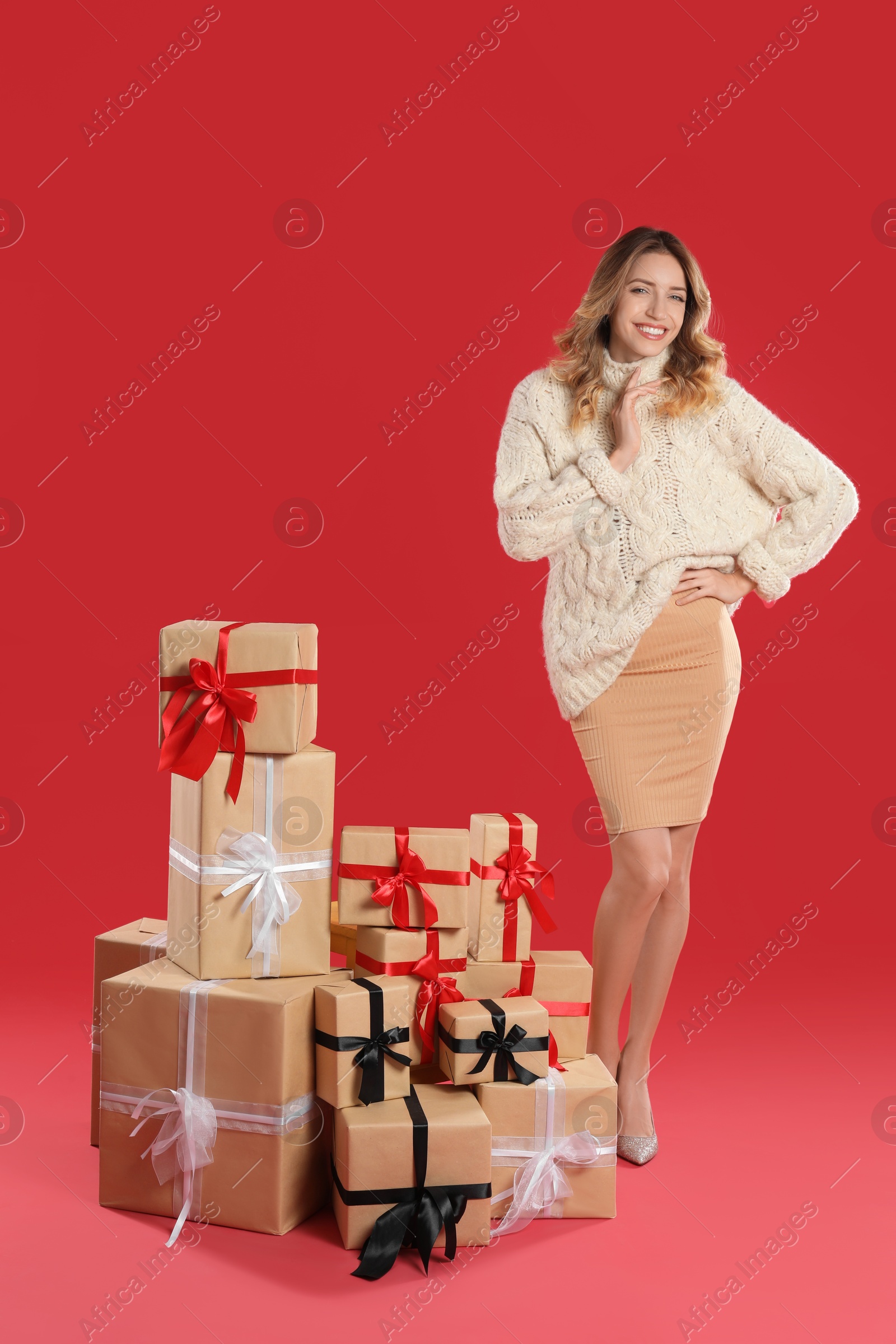 Photo of Beautiful young woman with pile of Christmas presents on red background