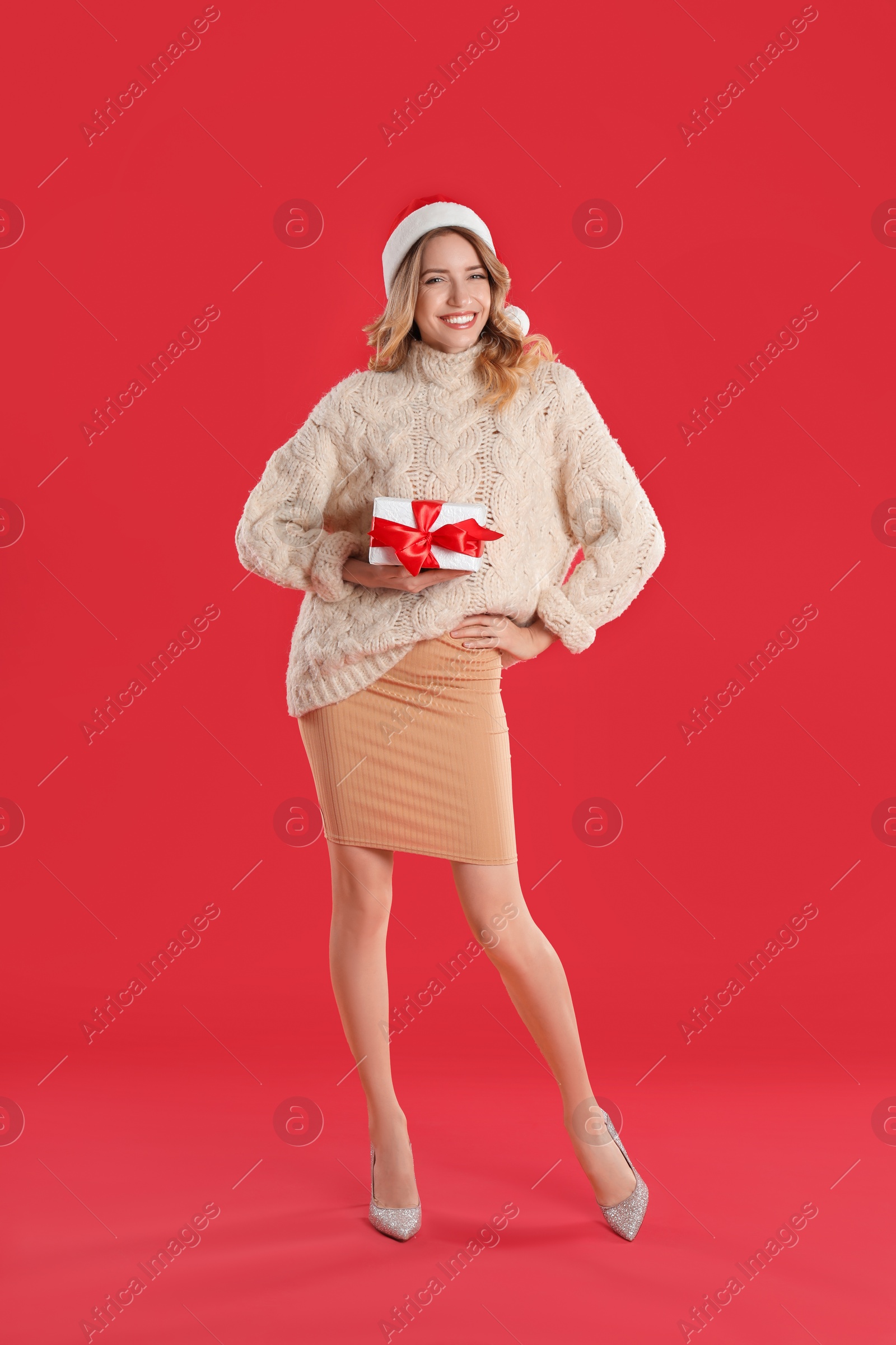 Photo of Beautiful young woman in Santa hat with Christmas present on red background