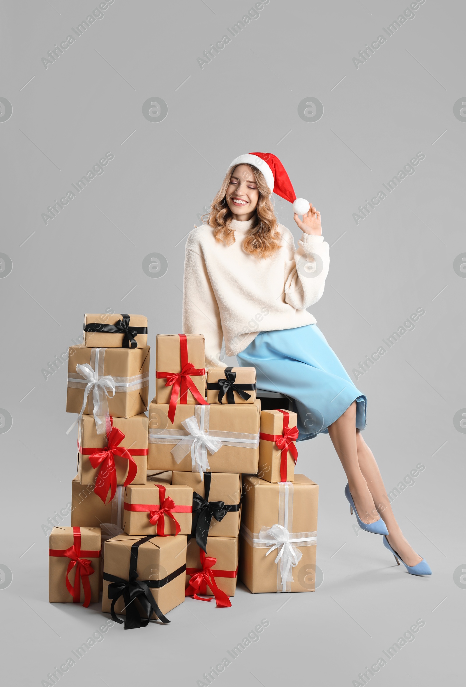 Photo of Beautiful young woman in Santa hat with pile of Christmas presents on light grey background