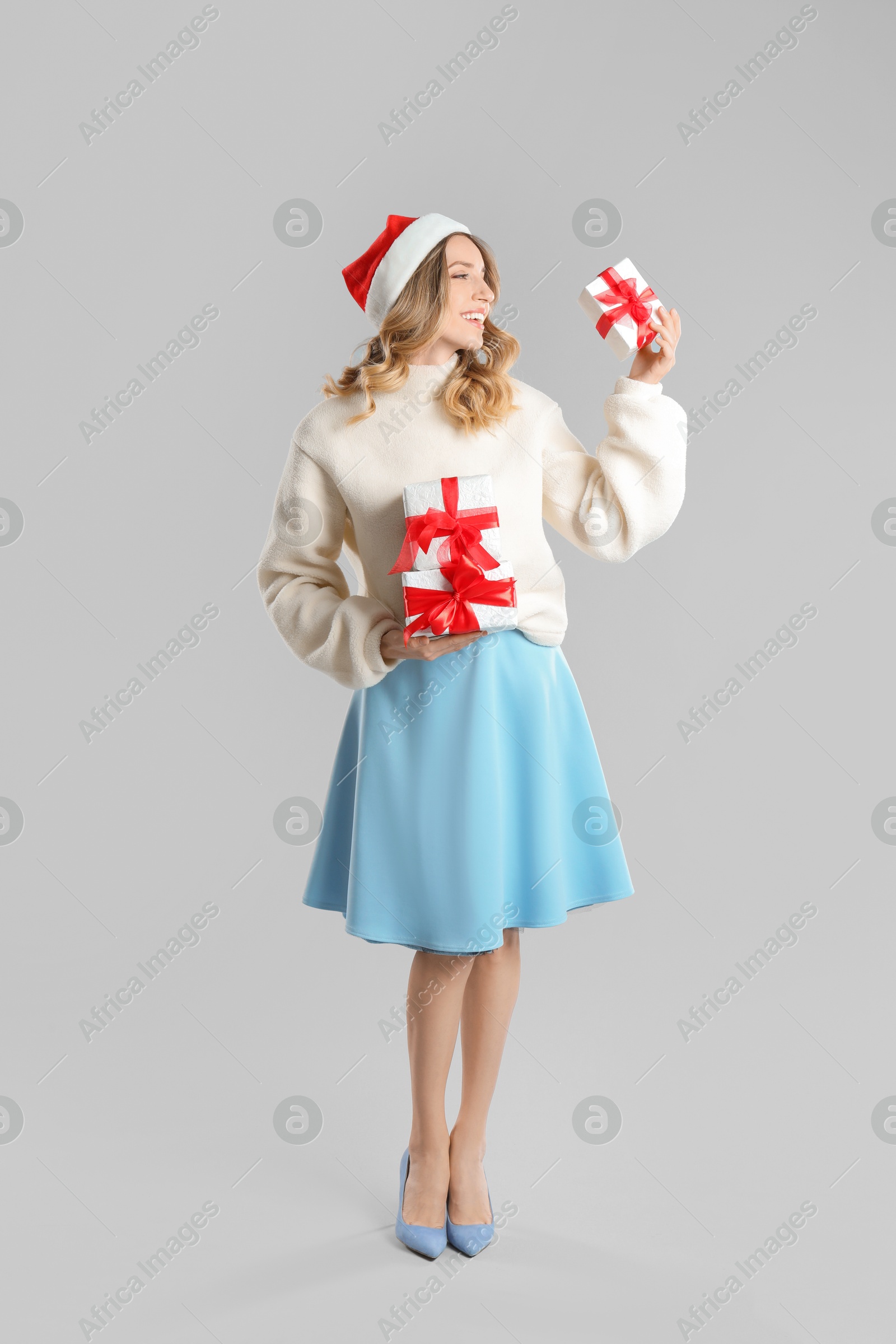 Photo of Beautiful young woman in Santa hat with Christmas presents on light grey background