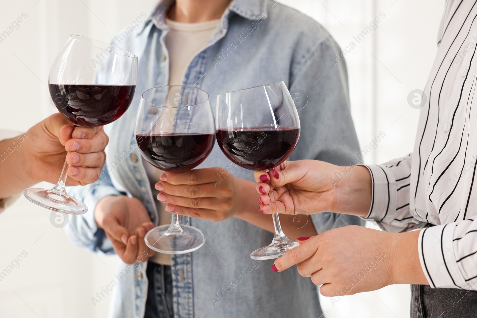 Photo of People clinking glasses of red wine indoors, closeup