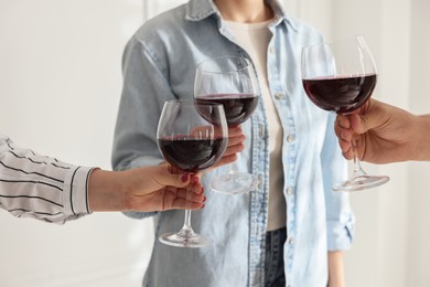 Photo of People clinking glasses of red wine indoors, closeup