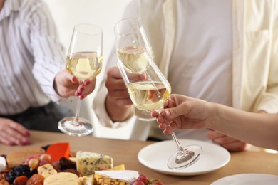 Photo of People clinking glasses of wine at served table, closeup