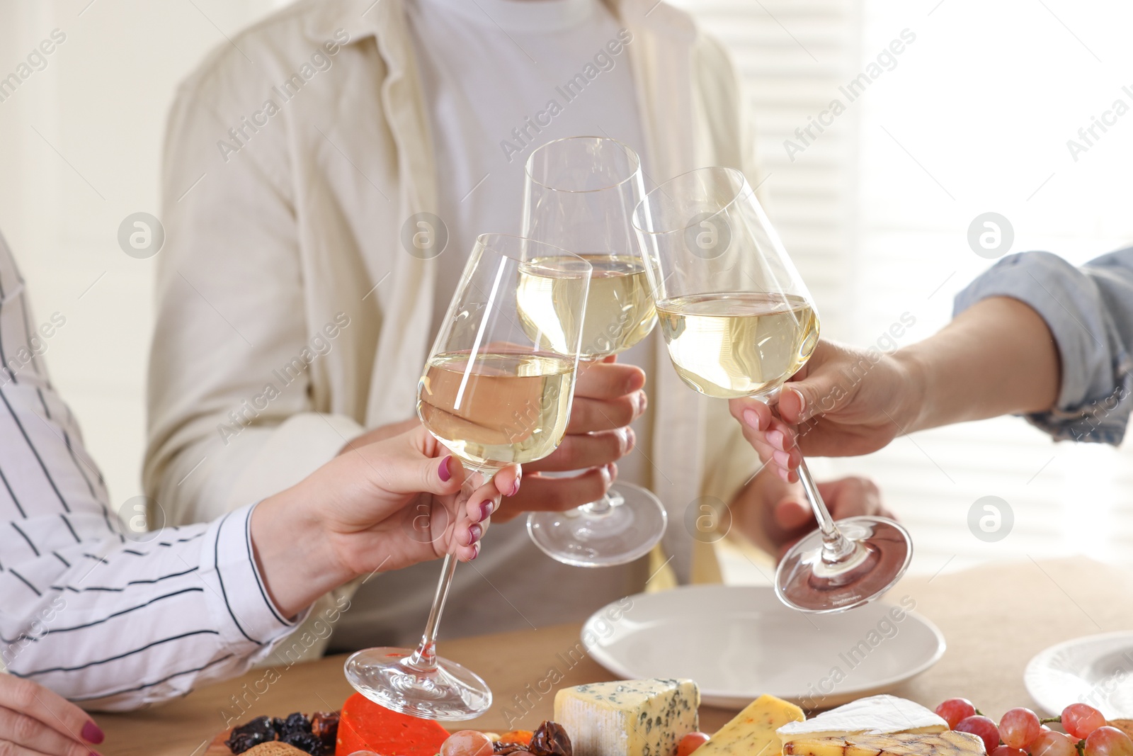 Photo of People clinking glasses of wine at served table, closeup