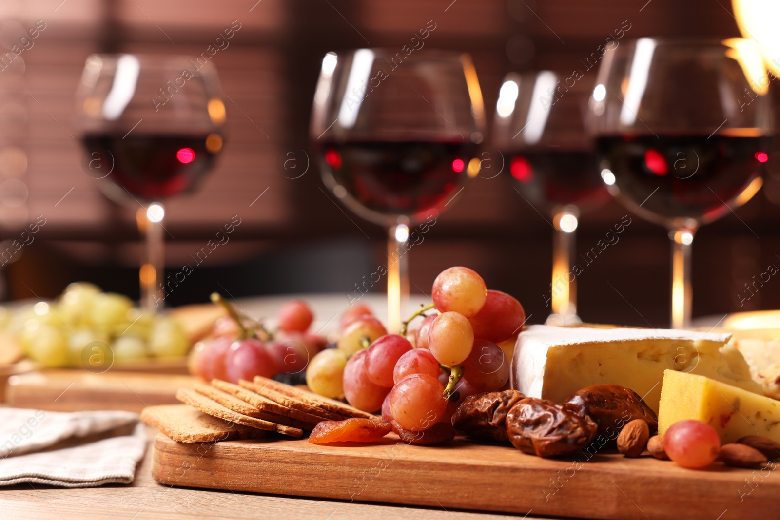 Photo of Glasses of red wine and different snacks on wooden table, selective focus