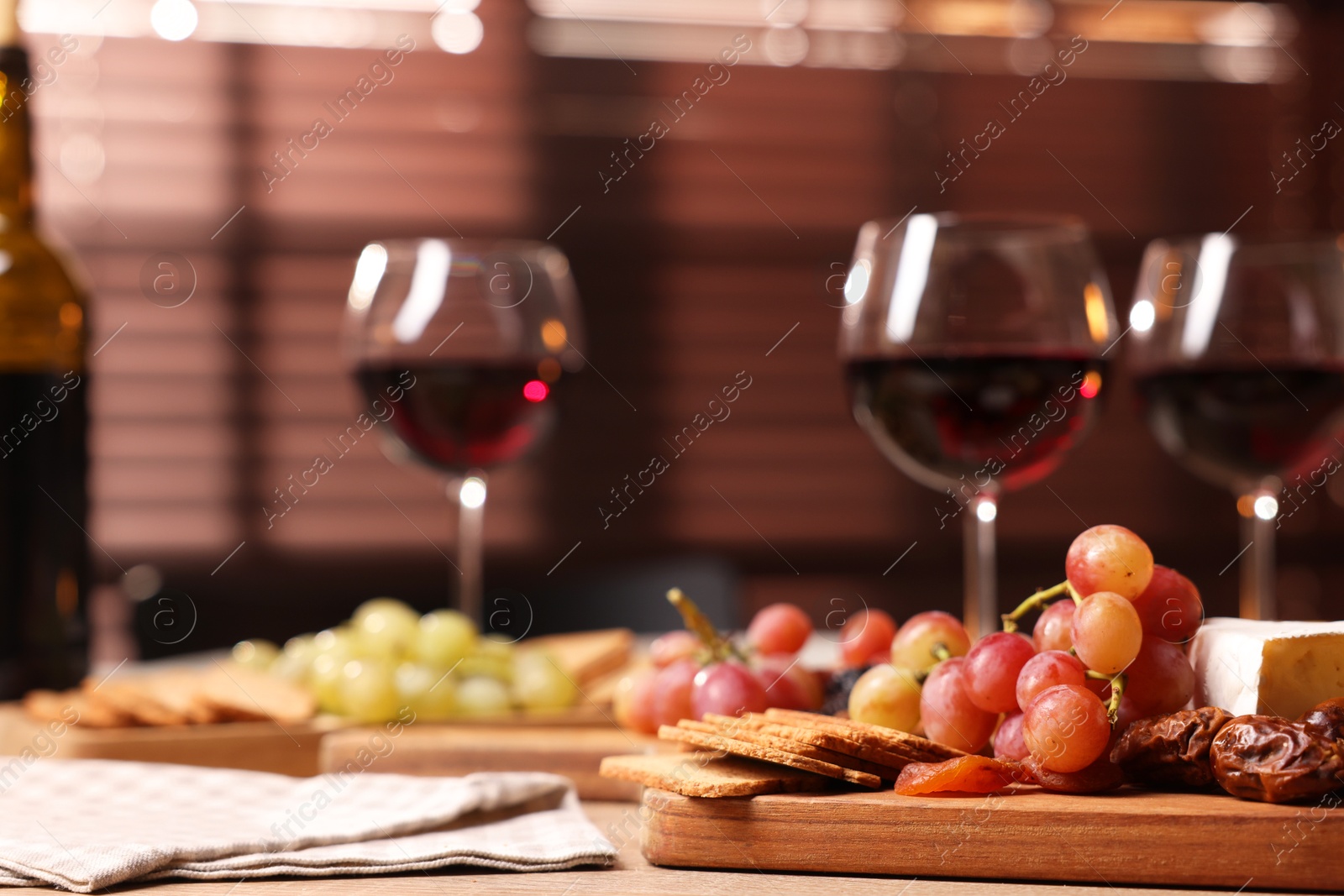 Photo of Glasses of red wine and different snacks on wooden table, selective focus. Space for text