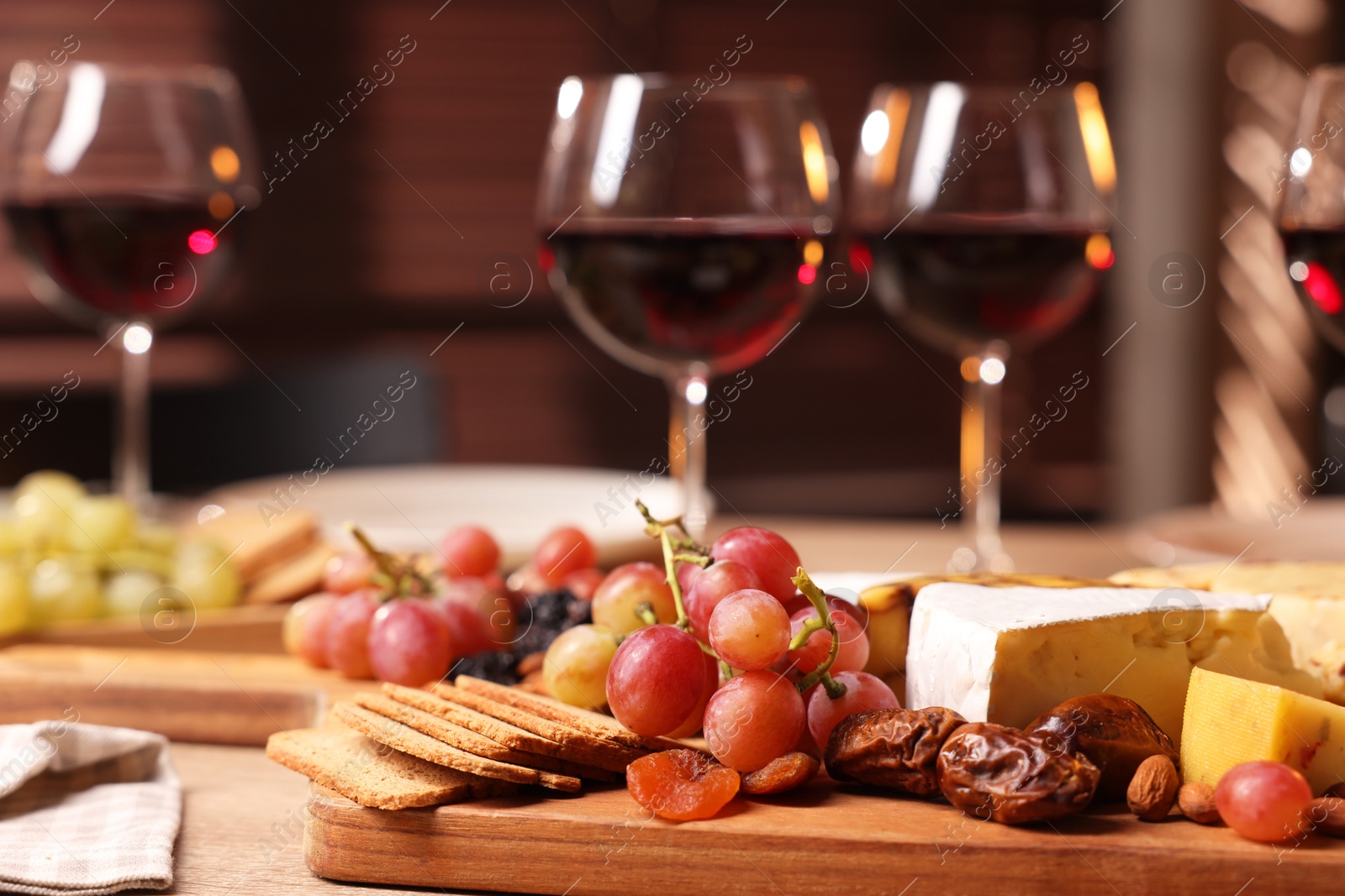 Photo of Glasses of red wine and different snacks on wooden table, selective focus