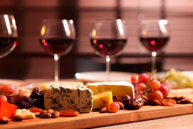 Photo of Glasses of red wine and different snacks on wooden table, selective focus