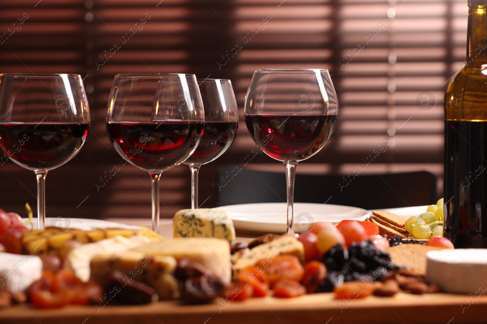 Photo of Glasses of red wine and different snacks on table, selective focus