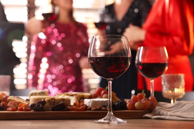 Photo of People holding glasses of wine at party, focus on wooden table with snacks and alcohol