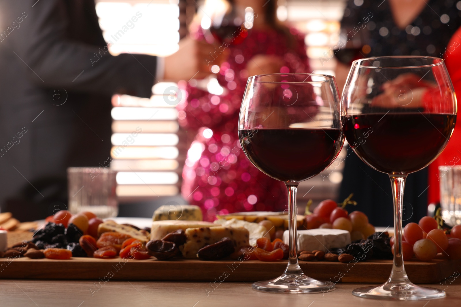 Photo of People holding glasses of wine at party, focus on wooden table with snacks and alcohol