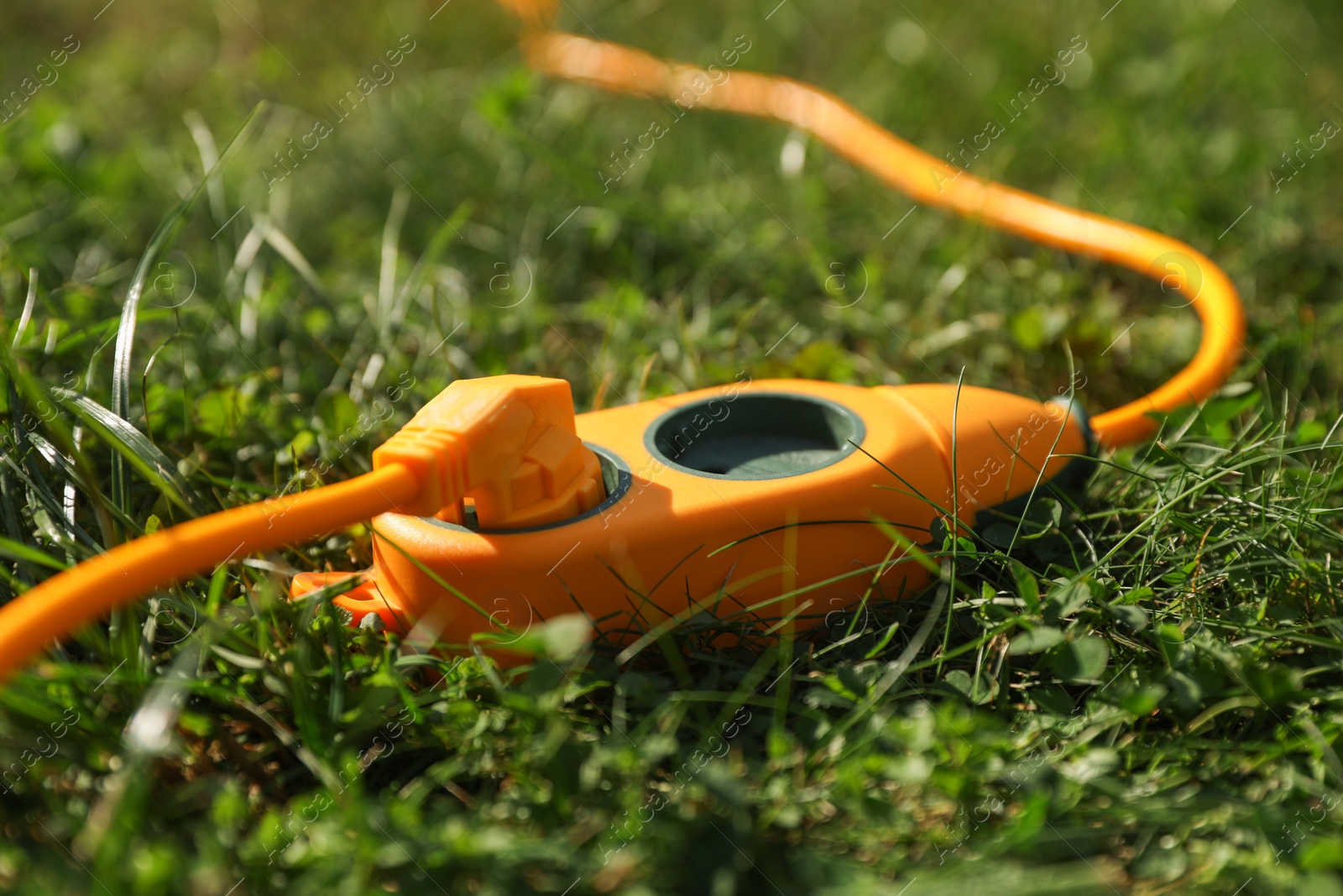 Photo of Orange extension cord on green grass outdoors, closeup