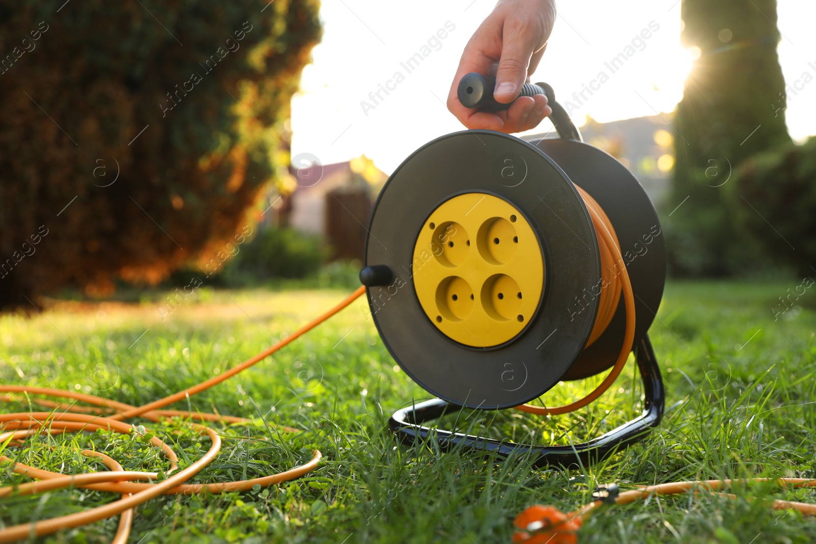 Photo of Man with extension cord reel on green grass outdoors, closeup