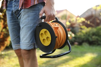 Photo of Man with extension cord reel outdoors on sunny day, closeup