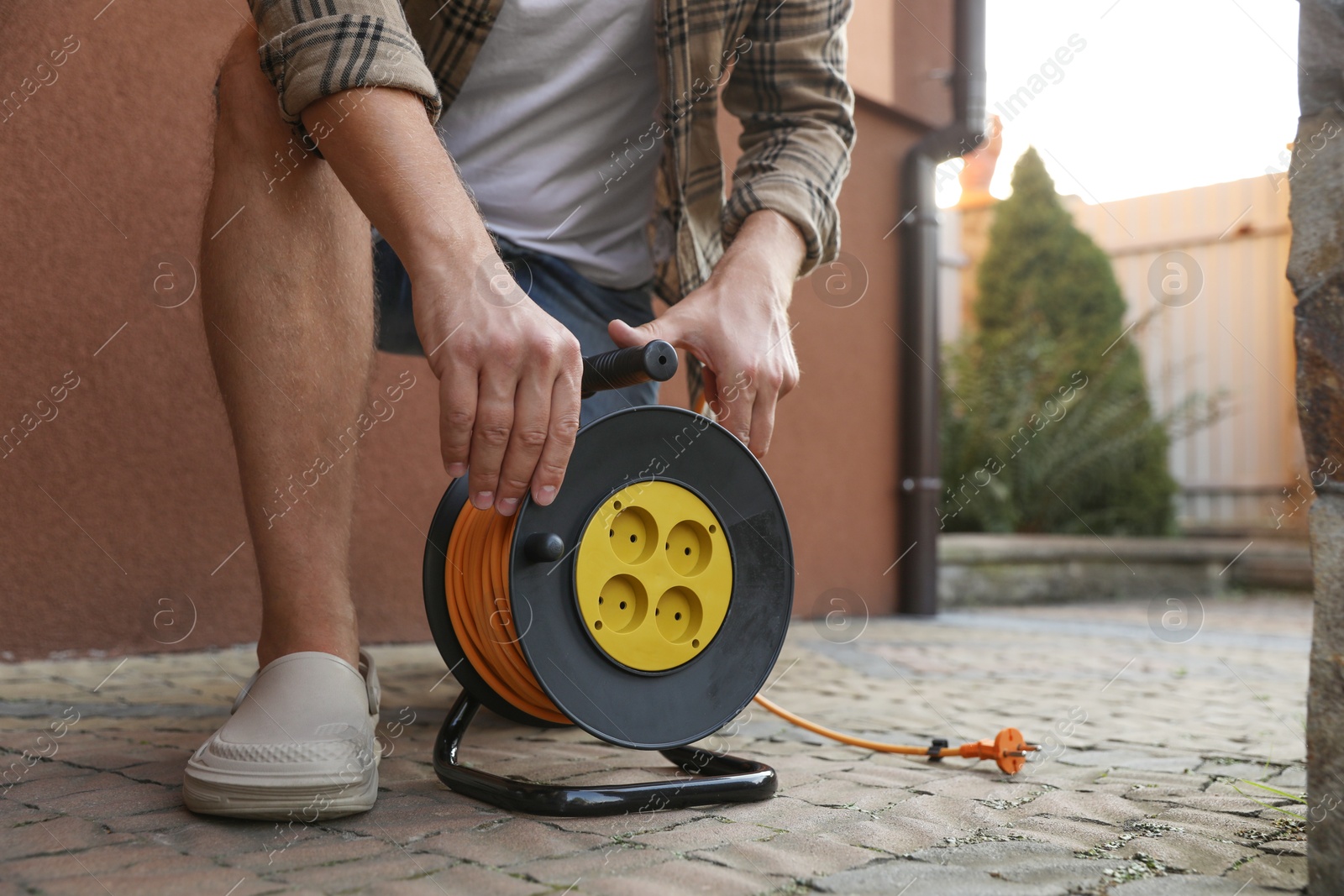 Photo of Man with extension cord reel in backyard, closeup. Space for text