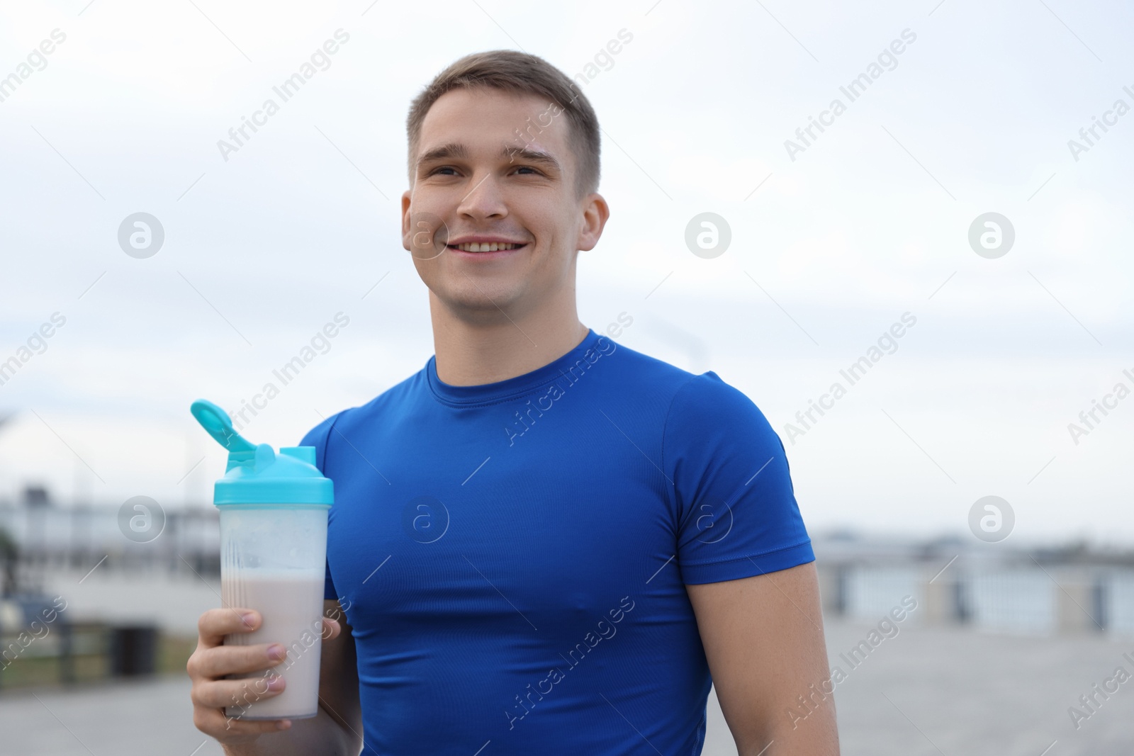 Photo of Smiling man with shaker of protein drink outdoors