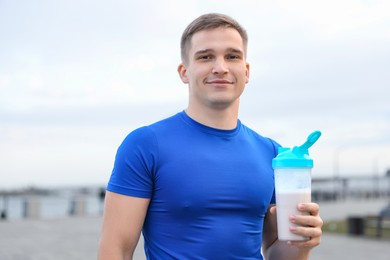 Athletic man with shaker of protein drink outdoors