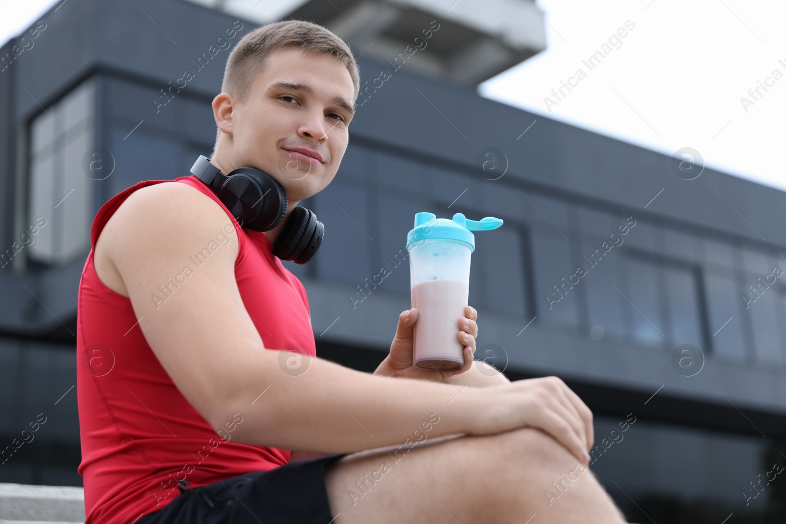 Photo of Athletic man with shaker of protein drink outdoors, low angle view