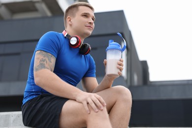 Athletic man with shaker of protein drink outdoors, low angle view