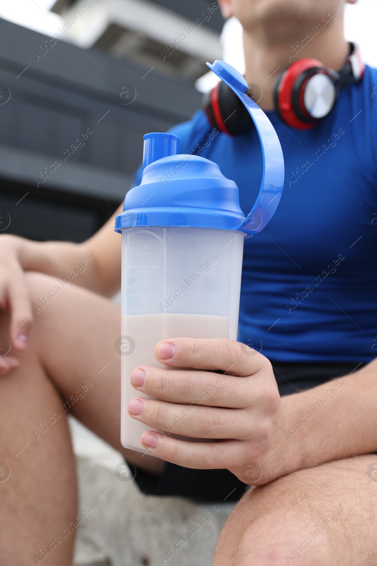 Photo of Athletic man with shaker of protein drink outdoors, closeup