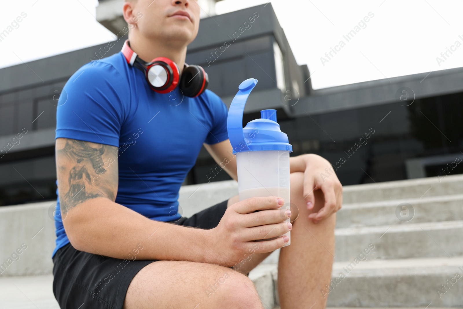 Photo of Athletic man with shaker of protein drink outdoors, closeup