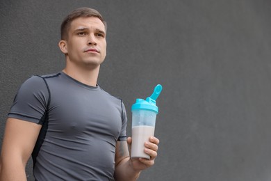 Photo of Athletic man with shaker of protein drink near grey wall, low angle view. Space for text