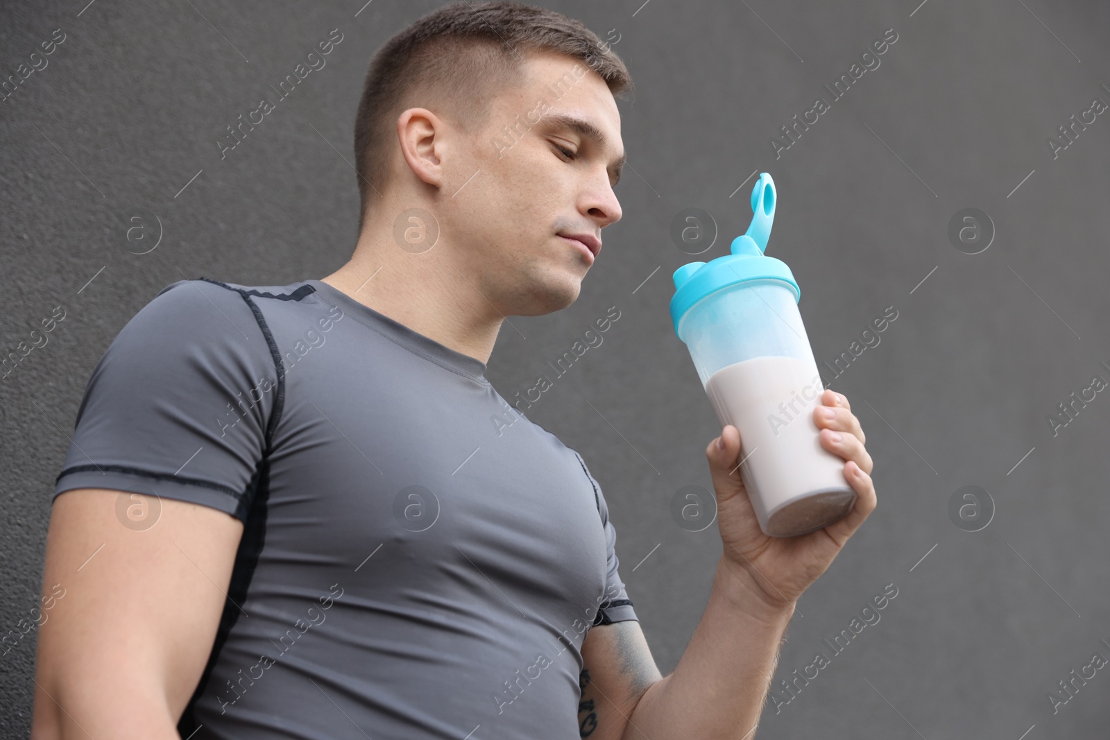 Photo of Athletic man drinking protein shake near grey wall, low angle view