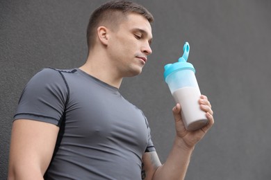 Photo of Athletic man drinking protein shake near grey wall, low angle view