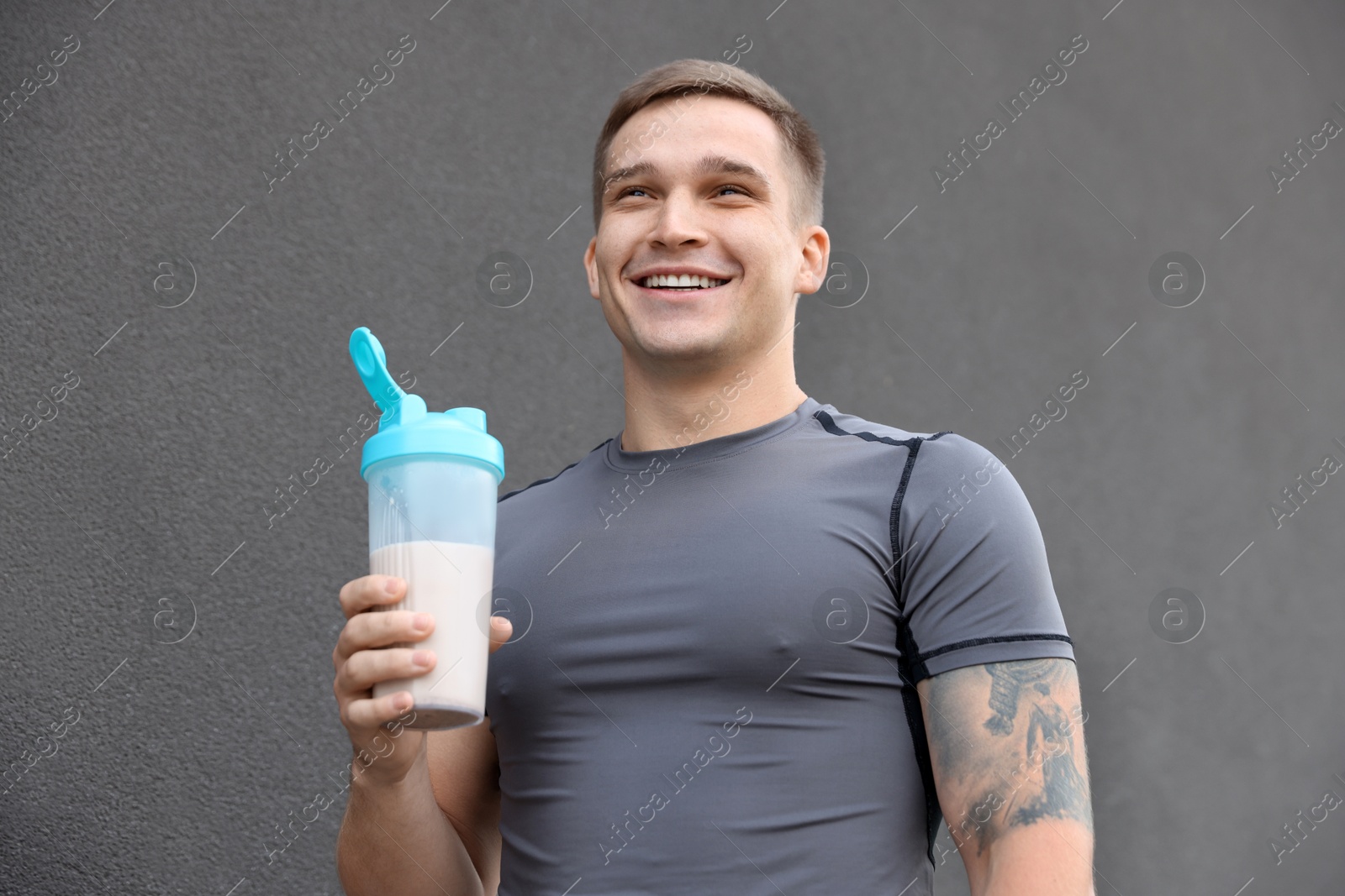 Photo of Smiling man with shaker of protein drink near grey wall