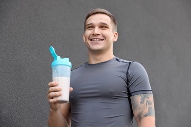 Photo of Smiling man with shaker of protein drink near grey wall