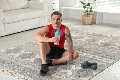 Photo of Athletic man with shaker of protein drink sitting on carpet at home