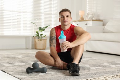 Photo of Athletic man with shaker of protein drink sitting on carpet at home