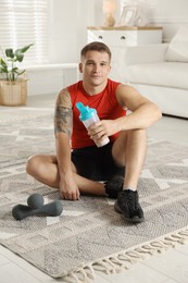 Photo of Athletic man with shaker of protein drink sitting on carpet at home